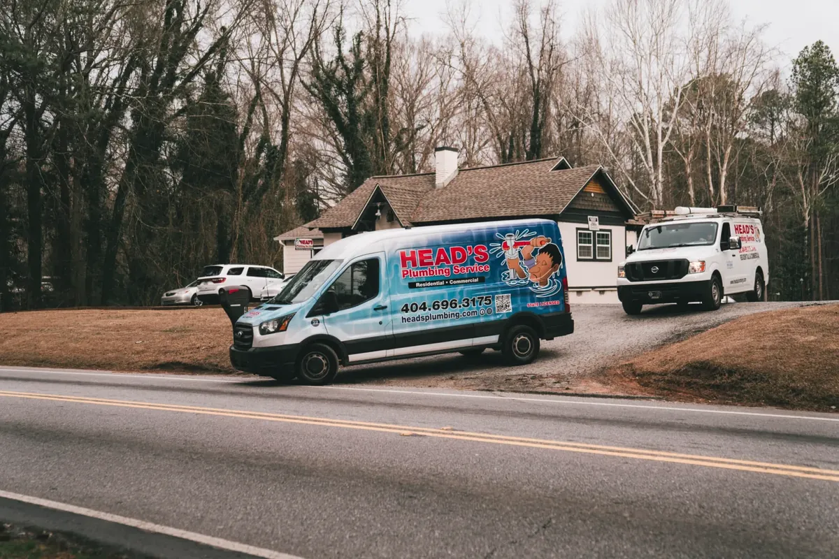 Two branded Head's Plumbing Service vans parked outside a metro Atlanta home
