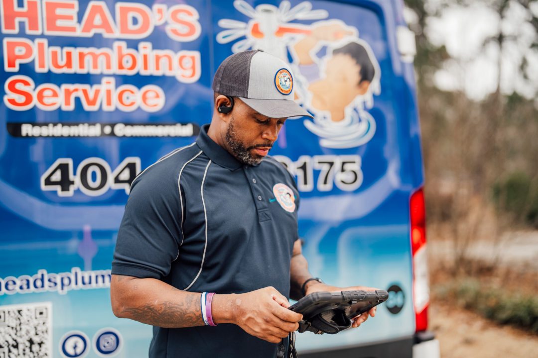 A Head's Plumbing technician reviewing the diagnostic on a tablet beside a branded service van