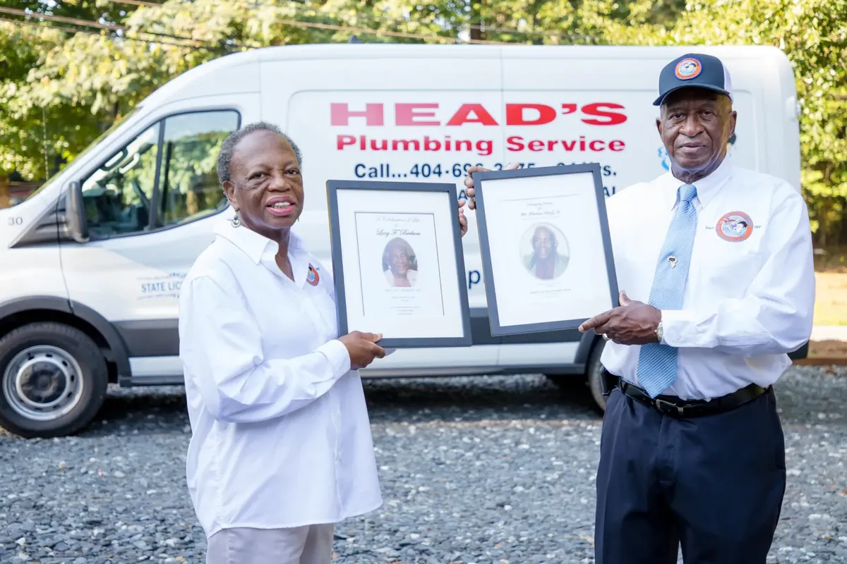 Head family in front of a Head's Plumbing van, holding framed tributes to founding generations.